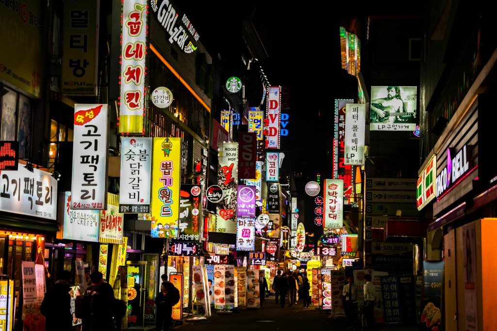Explore Seoul's vibrant nightlife on a bustling neon-lit street lined with shops and restaurants.